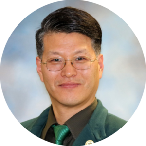 Headshot of Sung Soo Chung. He has short dark hair and wire frame glasses. He is wearing a dark green blazer