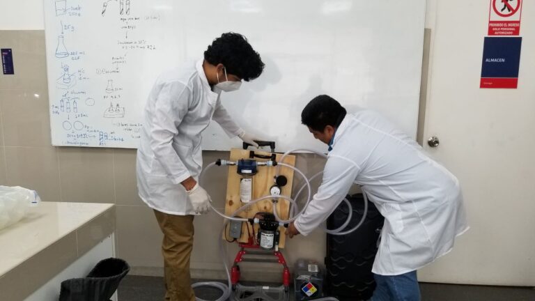 Two people looking at the machine in a classroom with lab coats on.
