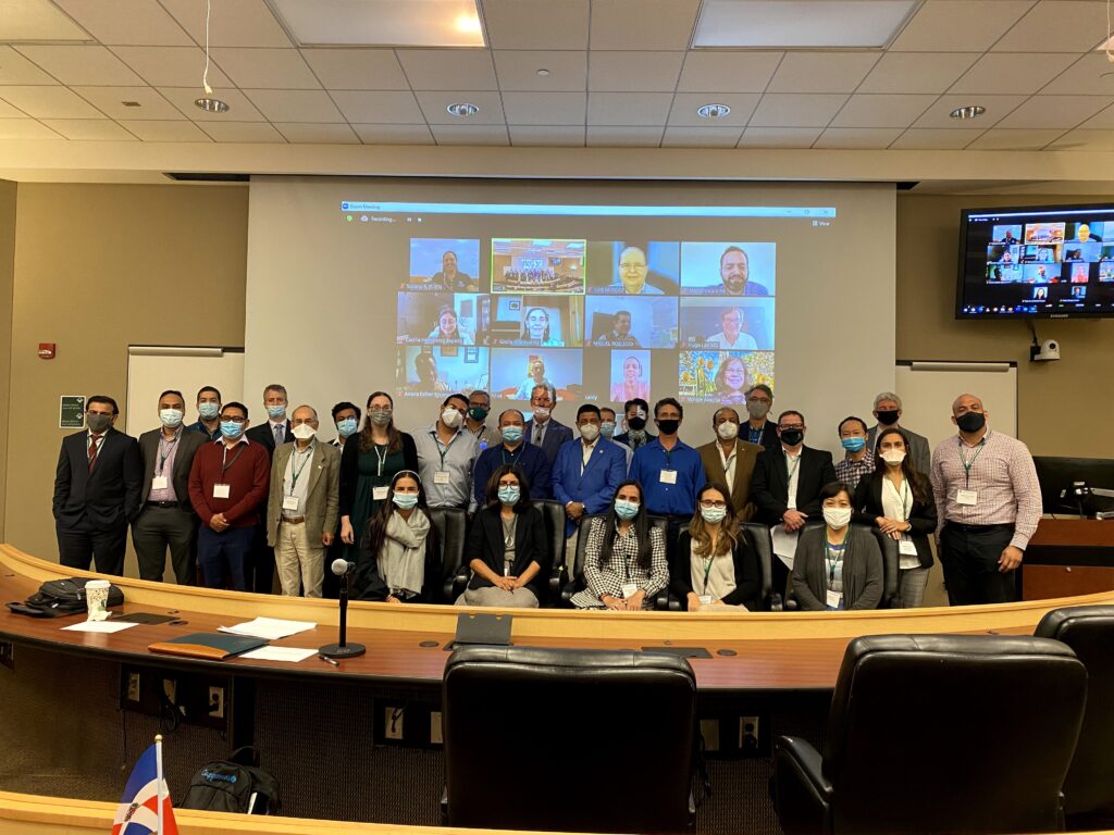 A photo from the 2021 ERCA conference of a large group of people in person standing in front of a large screen with people on zoom smiling for the picture