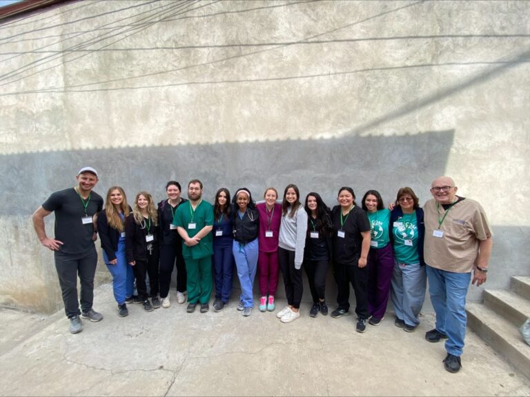 A group of people, some in scrubs, standing in front of a concrete wall