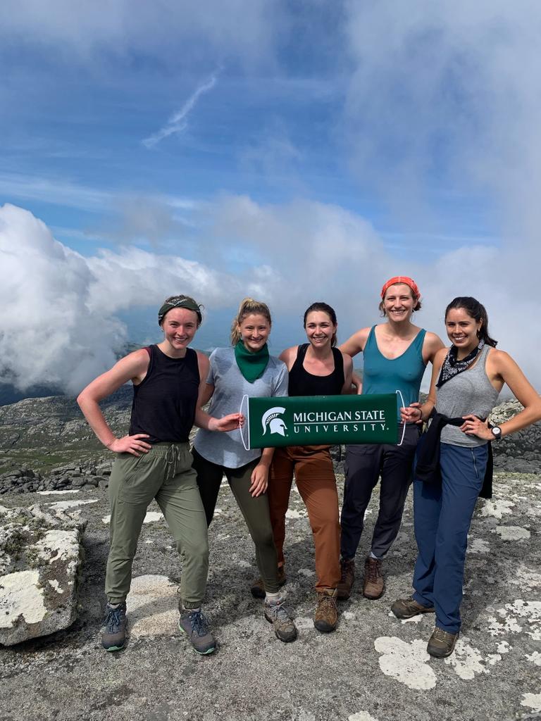 A group of people standing on top of a mountain holding an MSU banner