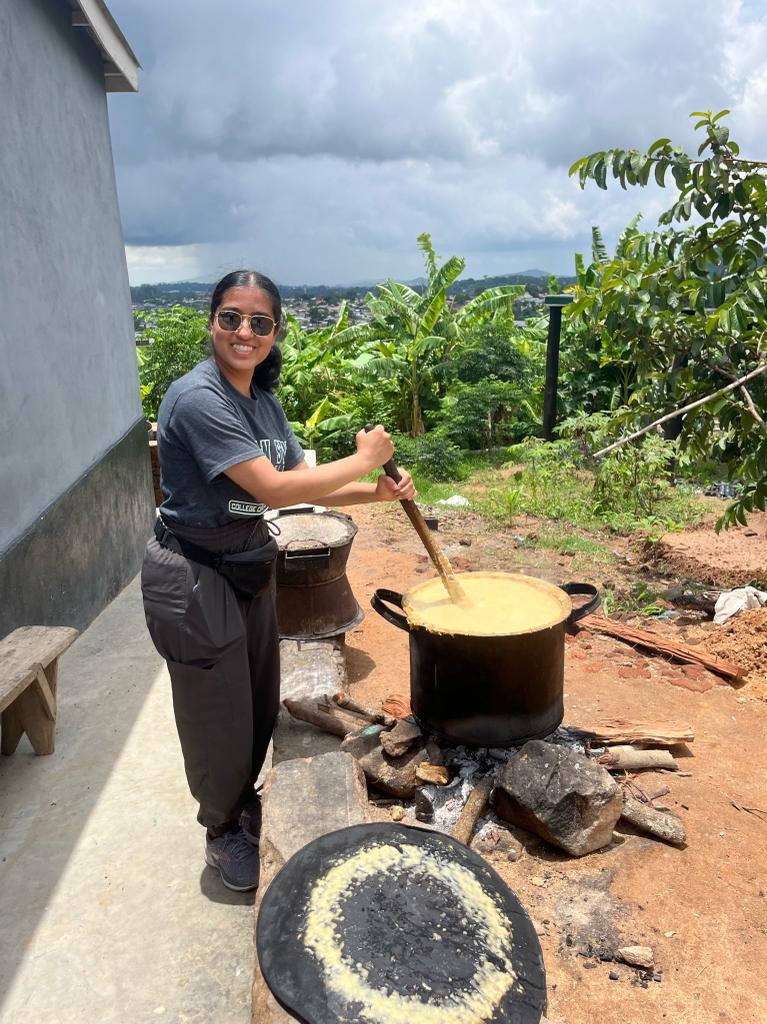 A woman making a big pot of food over a fire outside