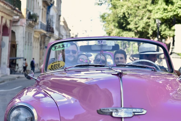 A group of people in an old pink classic car that is a taxi