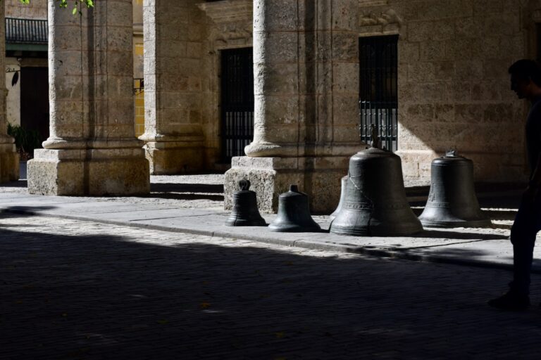 4 large old bells of various sizes next to a large marble column