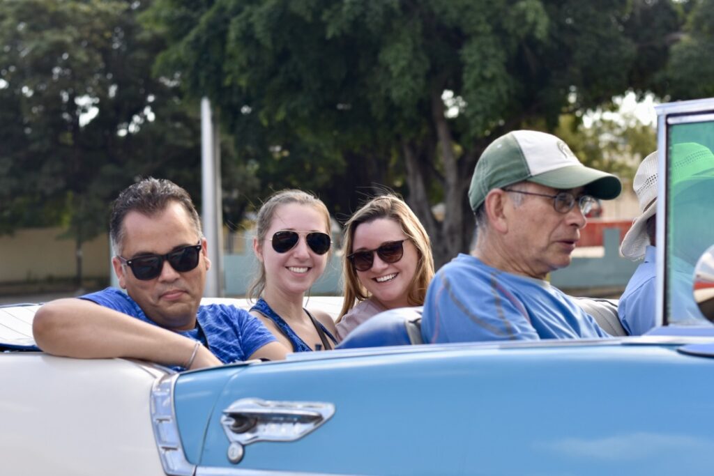 People smiling inside a blue convertible with the top down