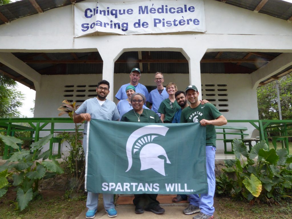 A group of people holding a Spartans Will flag outside a clinic building