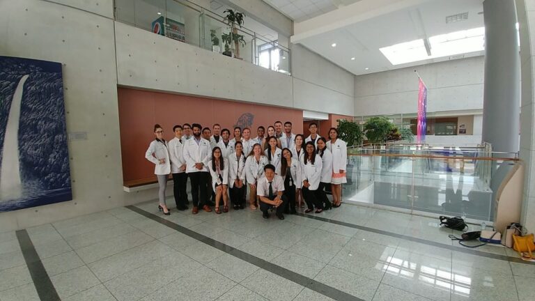 Group of people in white lab coats all smiling inside a building