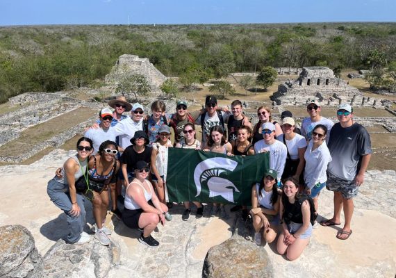 A group of students surrounding a MSU flag while on study abroad